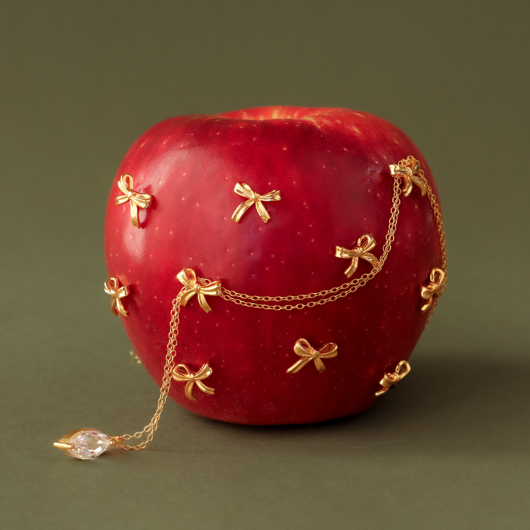 A womans ear with green and gold earrings, seen through sheer beige fabric, hand with green nails below.