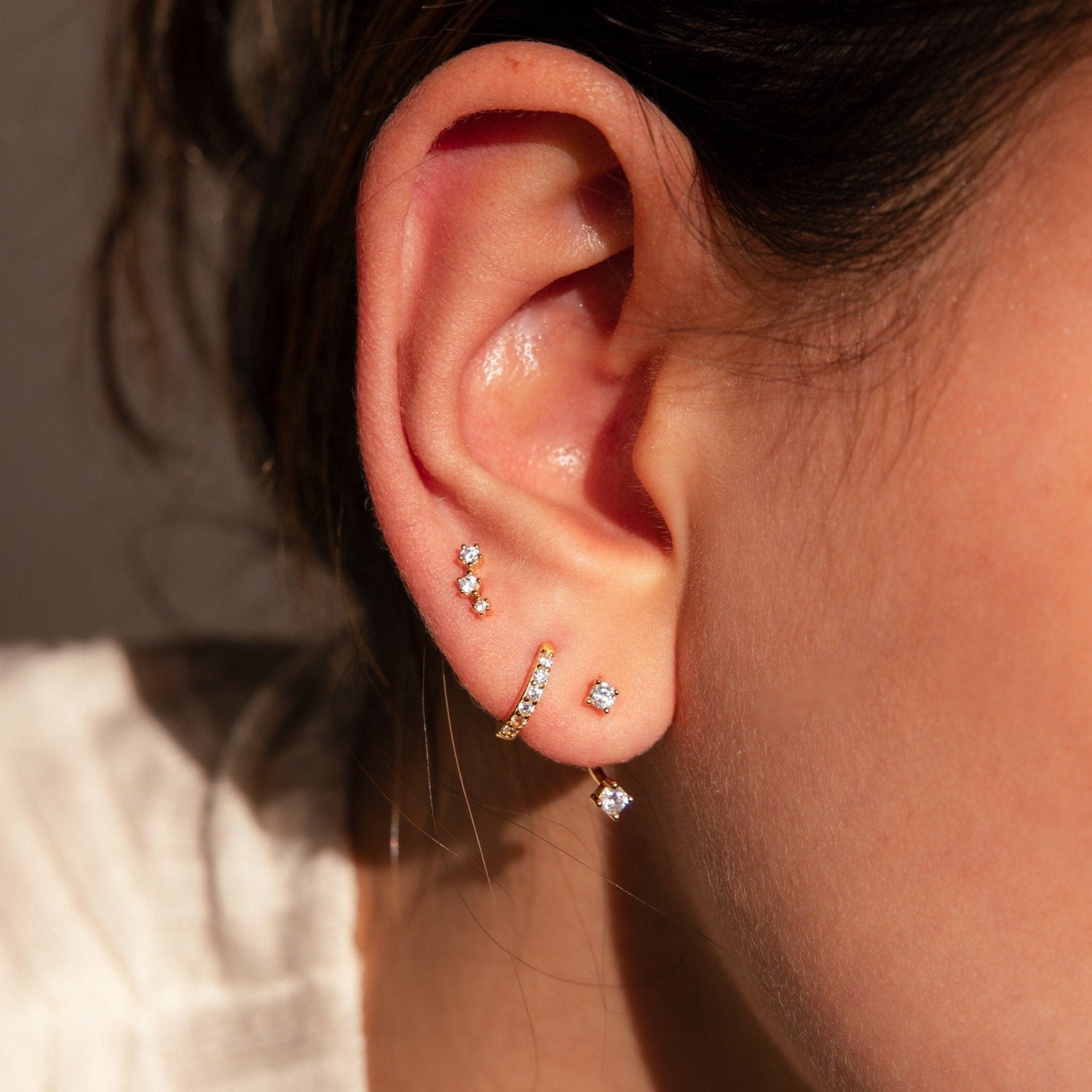 Close-up of an ear with four gold and diamond earrings in various piercings, against a neutral background.