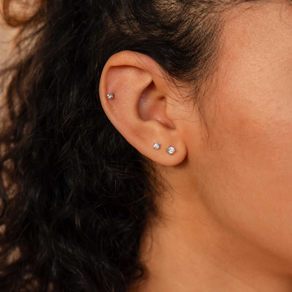 Close-up of an ear with three small diamond stud earrings and a Diamond Flatback Stud from the Diamond Flatback Studs Set in Sterling Silver, plus a variety of styles perfect for layering.