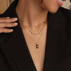 A close-up of a woman wearing a minimalist black blazer and the Onyx Necklace Set, featuring layered gold and onyx necklaces, highlights her neck and hand.