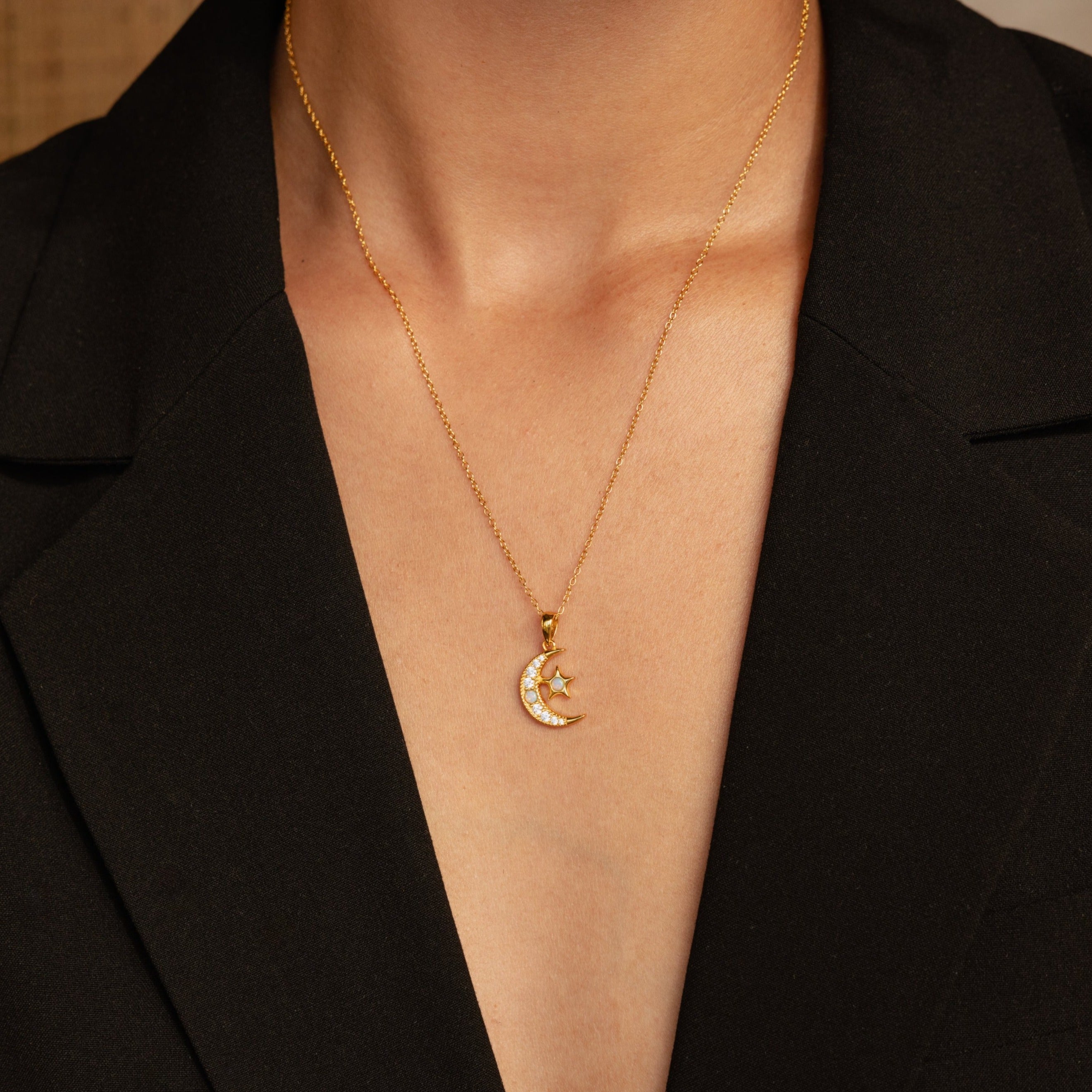 The Opal Moon & Star Necklace features a crescent moon and star pendant, shown styled with a black V-neck blazer.
