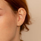 Close-up of an ear adorned with the Dainty Opal Stud Earrings Set—minimalist opal studs paired with a gold hoop featuring a dangling chain for an elegant, modern jewelry look.