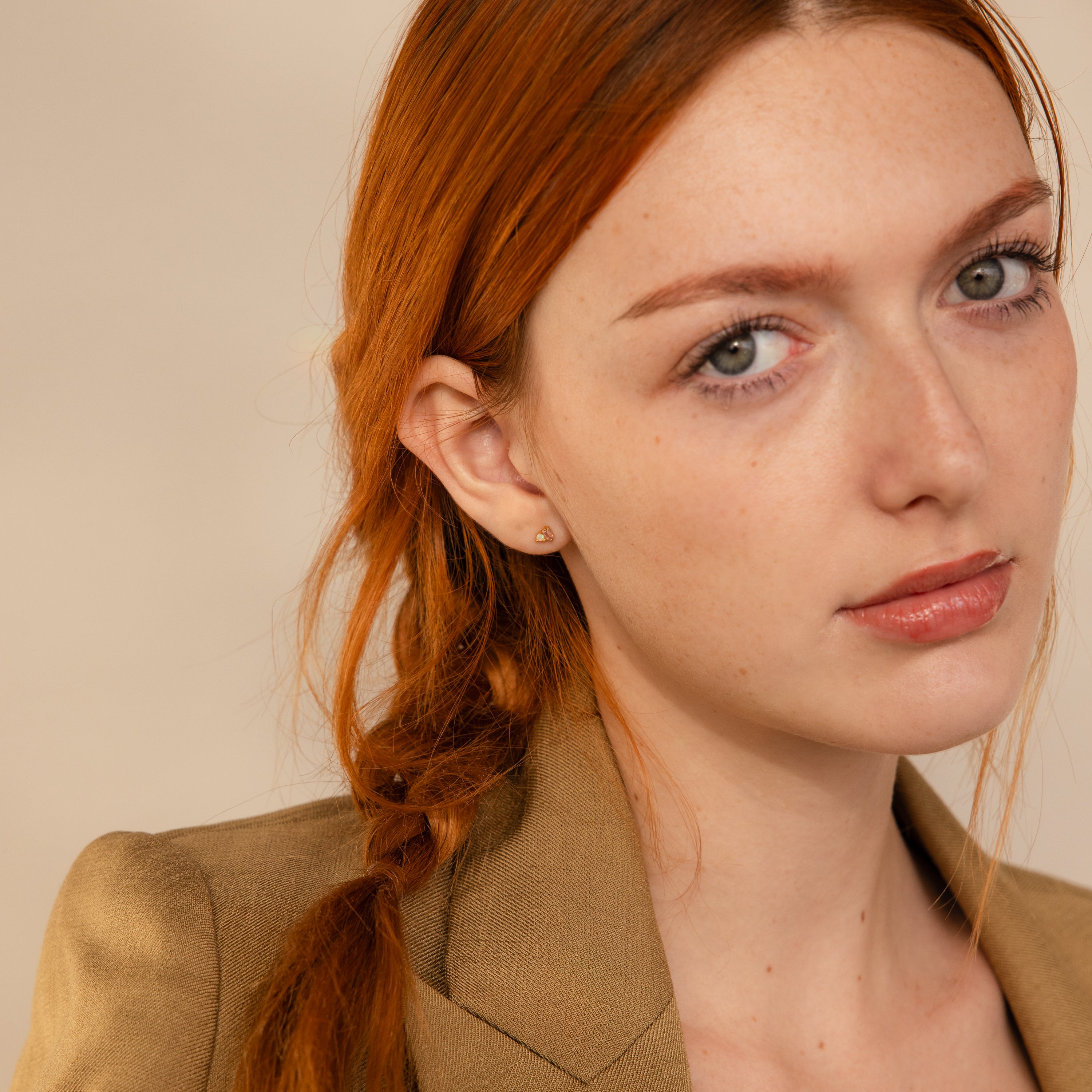 Young woman with red hair in a braid, wearing a tan blazer and Pink Baguette Opal Studs, looking at the camera with a neutral expression.