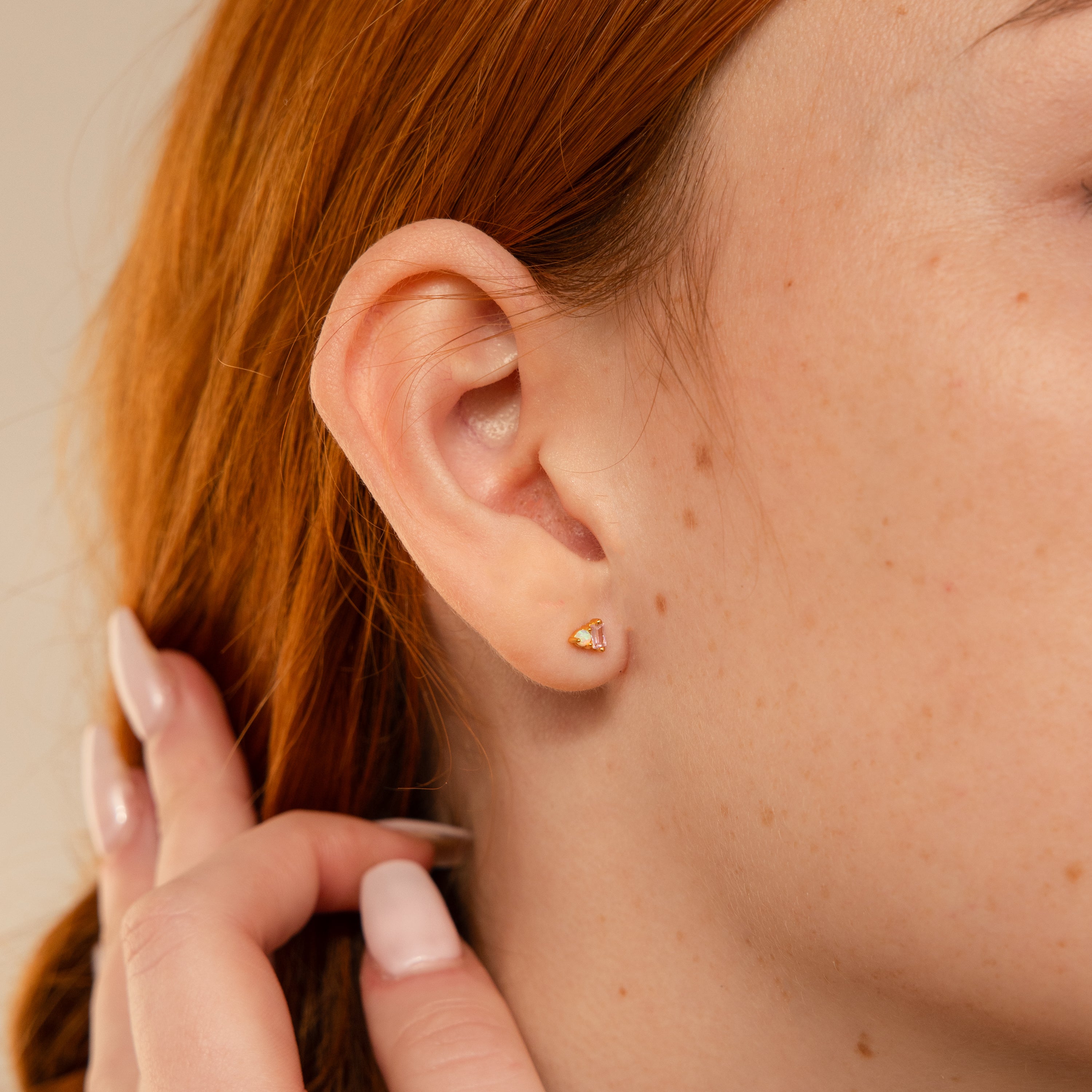 Close-up of a womans ear wearing Pink Baguette Opal Studs, her hand touching her hair with long nails—an elegant accessory, perfect as a bridal gift.