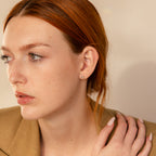 Young woman with red hair and light skin in a tan blazer, looking to the side with a neutral expression, showcasing elegant Pink Baguette Opal Studs.