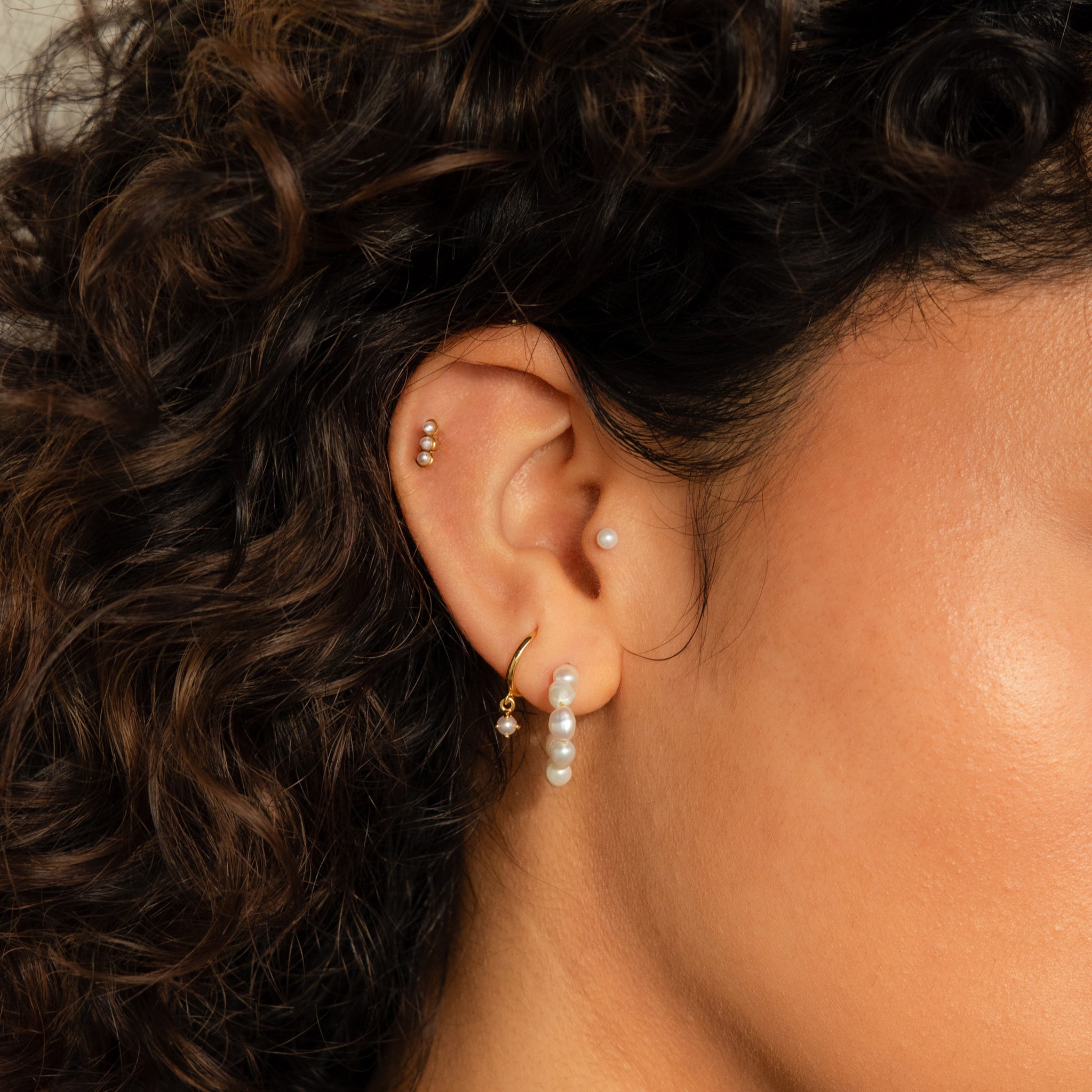 Close-up of a woman with curly hair wearing the Pearl Earrings Set, featuring stunning pearls and gold accents.