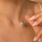 A person holding the Pearl Hummingbird Necklace in Sterling Silver, featuring an oval pendant with a delicate line drawing design.
