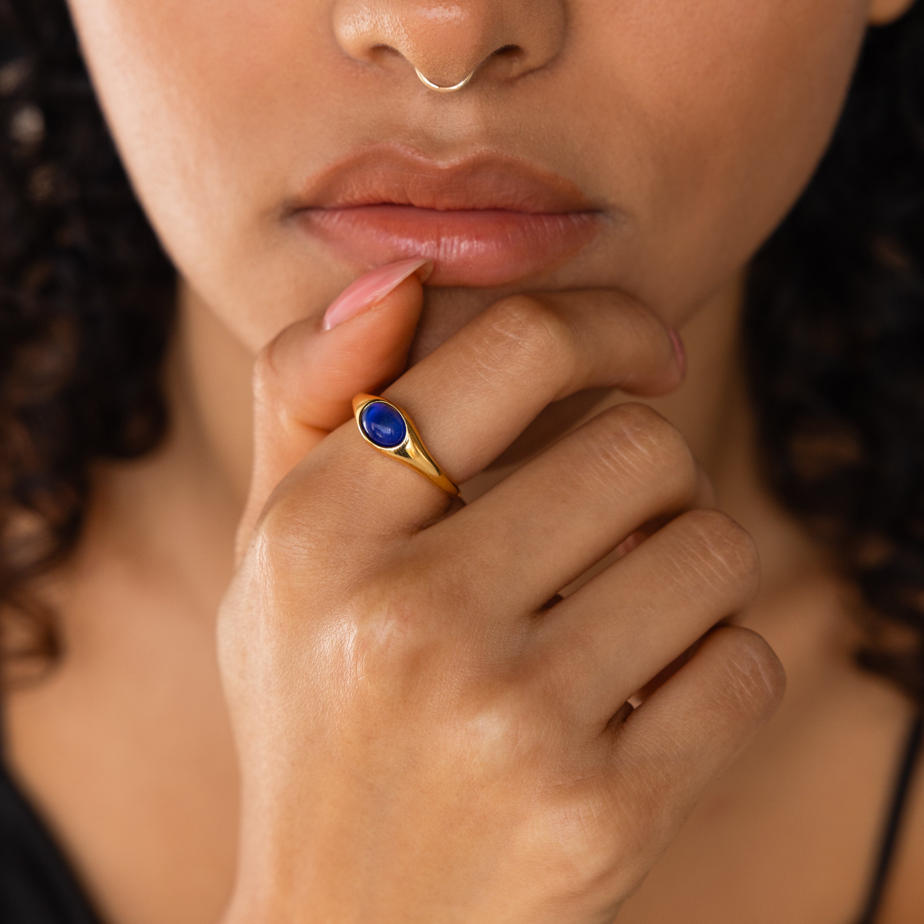 Woman wearing a Signet Mood Rings Set with a gold band and blue stone, touching her chin and showcasing nostalgic color-changing jewelry for mood ring lovers.
