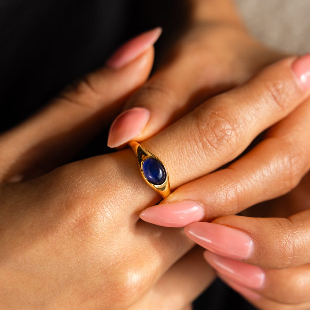 A hand with pink nails wears the Bold Mood Ring, featuring a dark blue oval stone and sculptural silhouette on the ring finger.