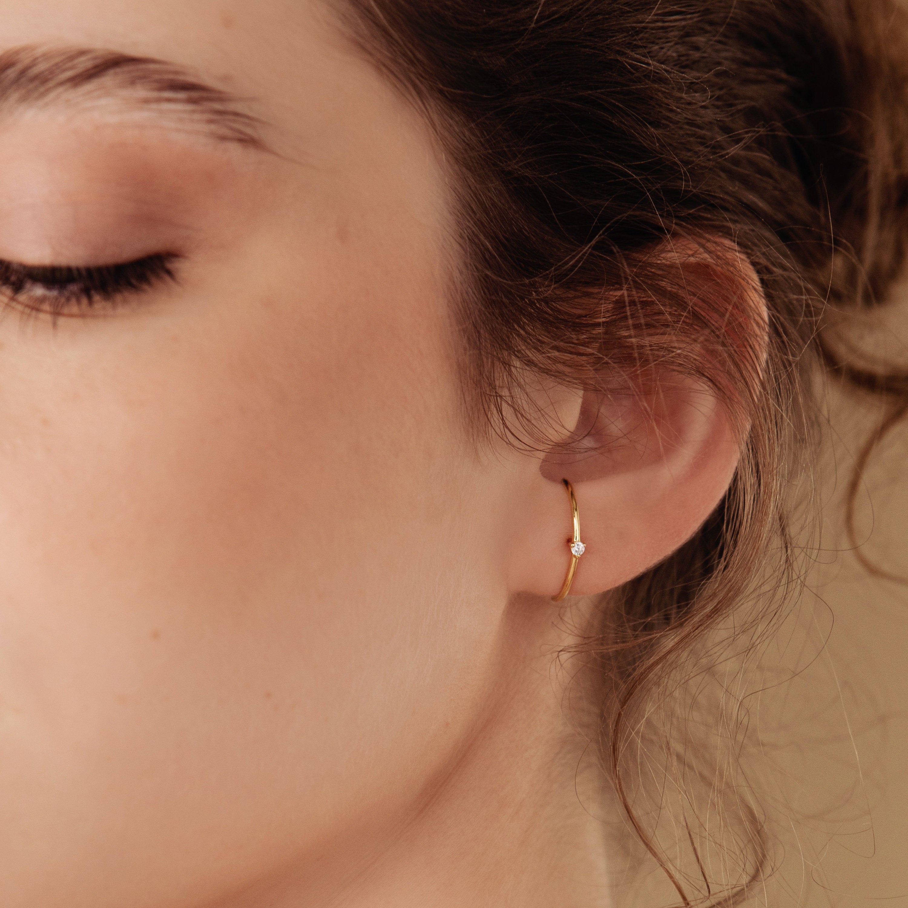 Close-up of a woman's ear wearing a gold hoop jacket earring with a diamond.