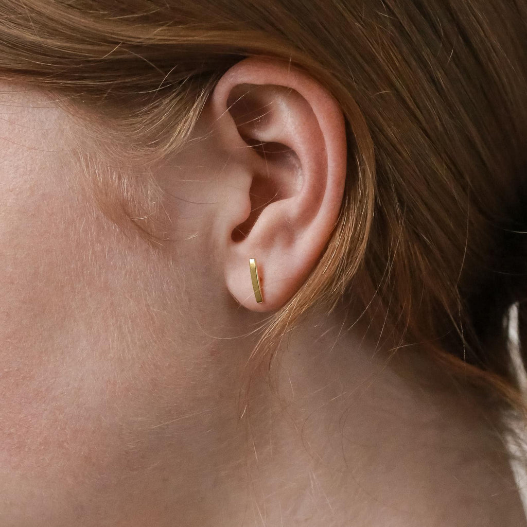 Close-up of a model wearing a gold bar stud earring with hair partially covering the frame.