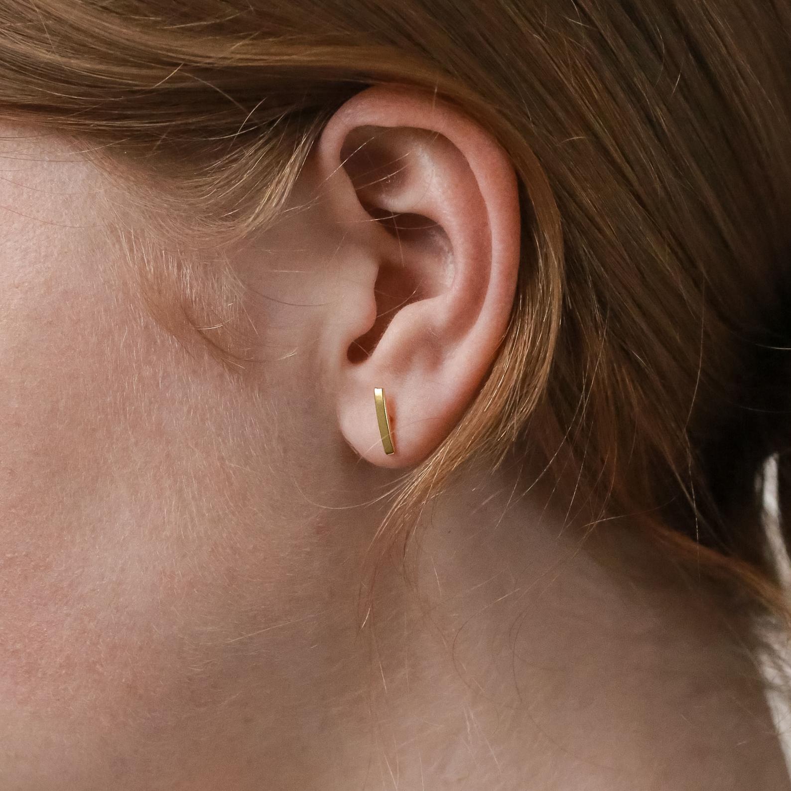 Close-up of a model wearing a gold bar stud earring with hair partially covering the frame.