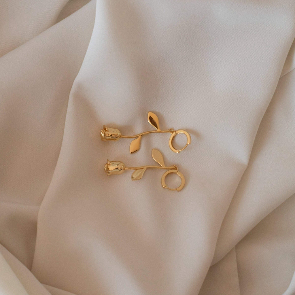 Gold rose earrings on a beige fabric background