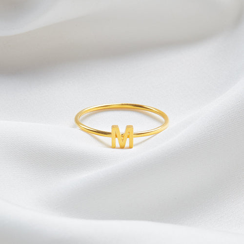 Gold ring with letter 'M' on a white satin background