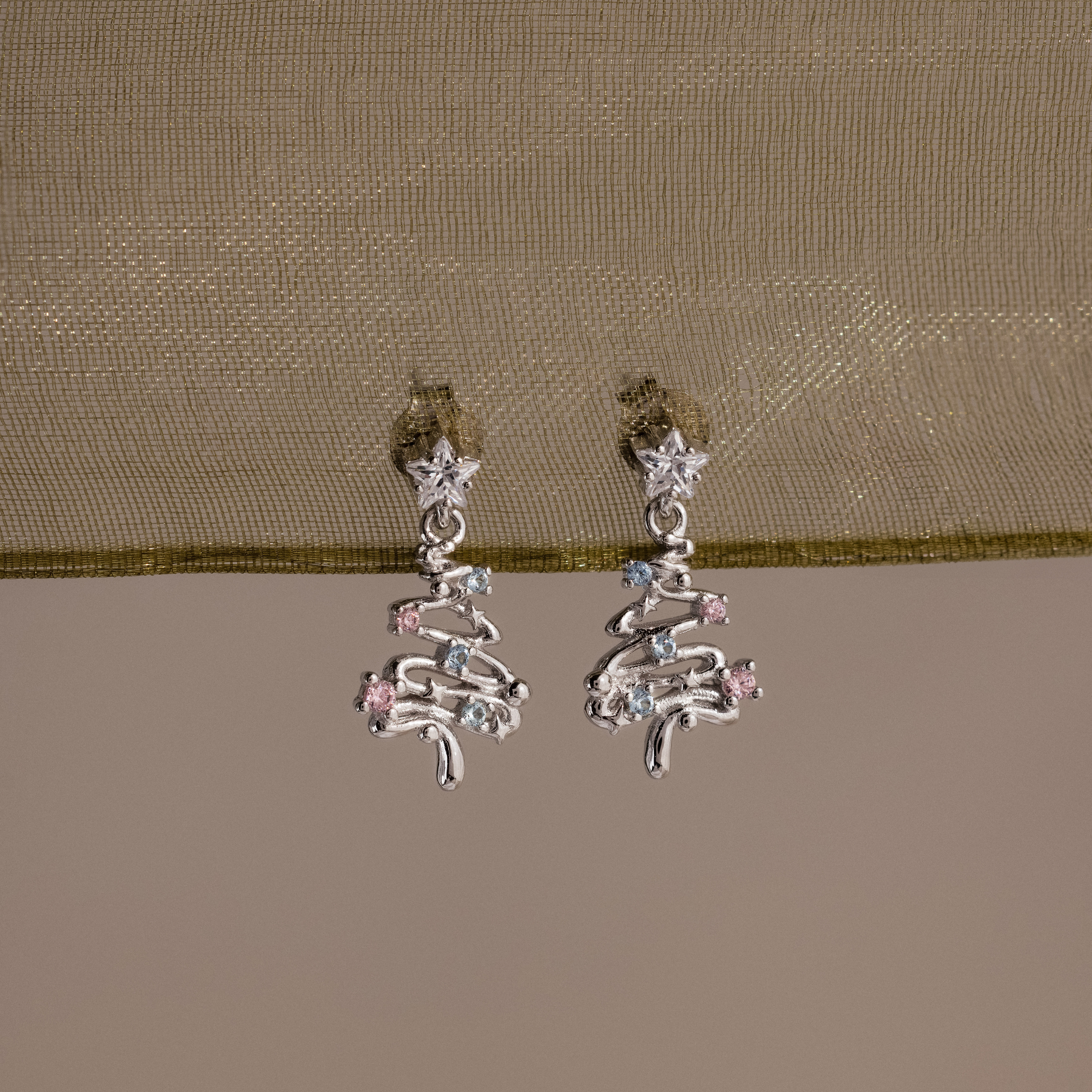 Silver Christmas tree earrings with gemstones on a beige fabric background