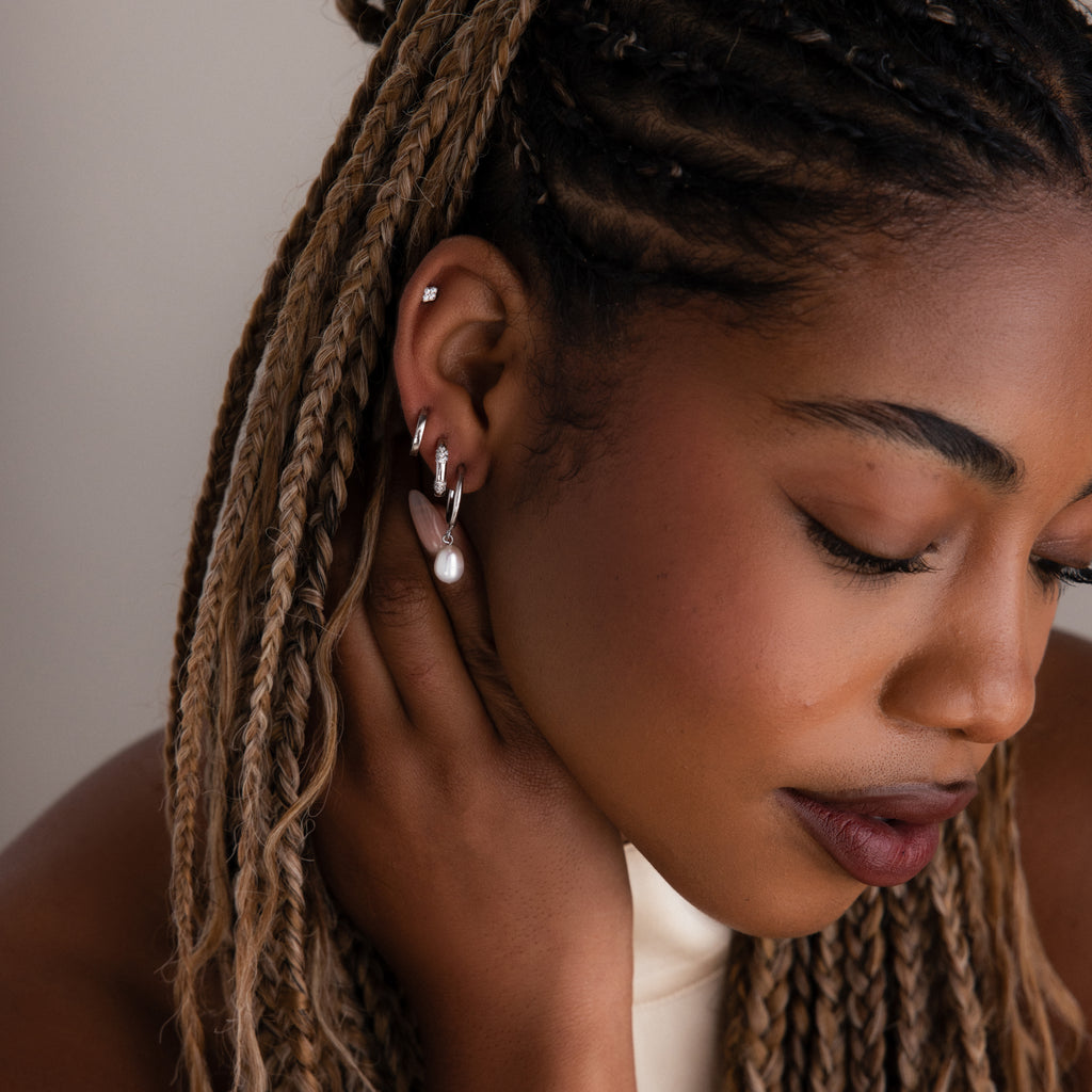 Close-up of a woman with braided hair wearing multiple silver earrings against a neutral background