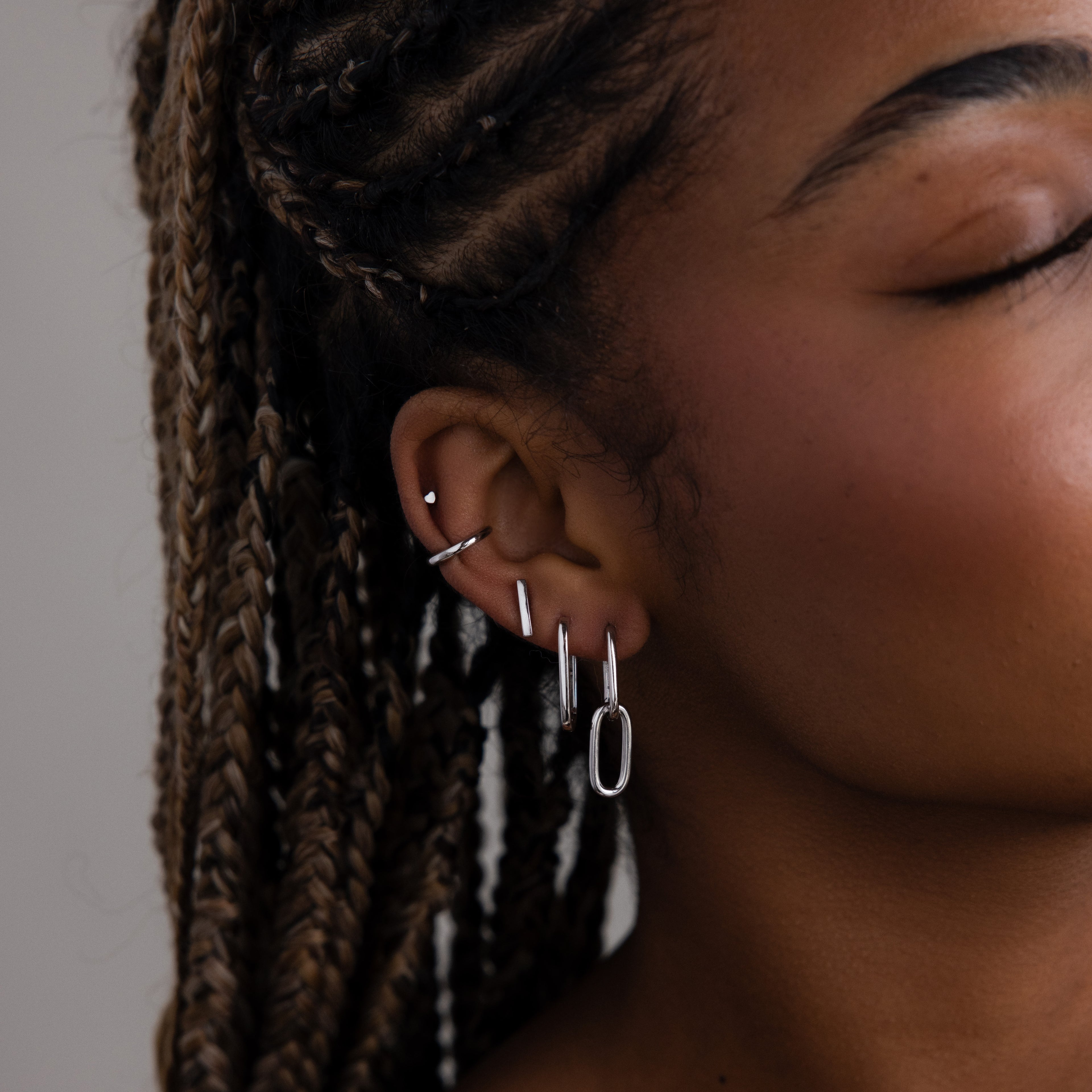 Close-up of a women's ear with multiple silver earrings against a neutral background
