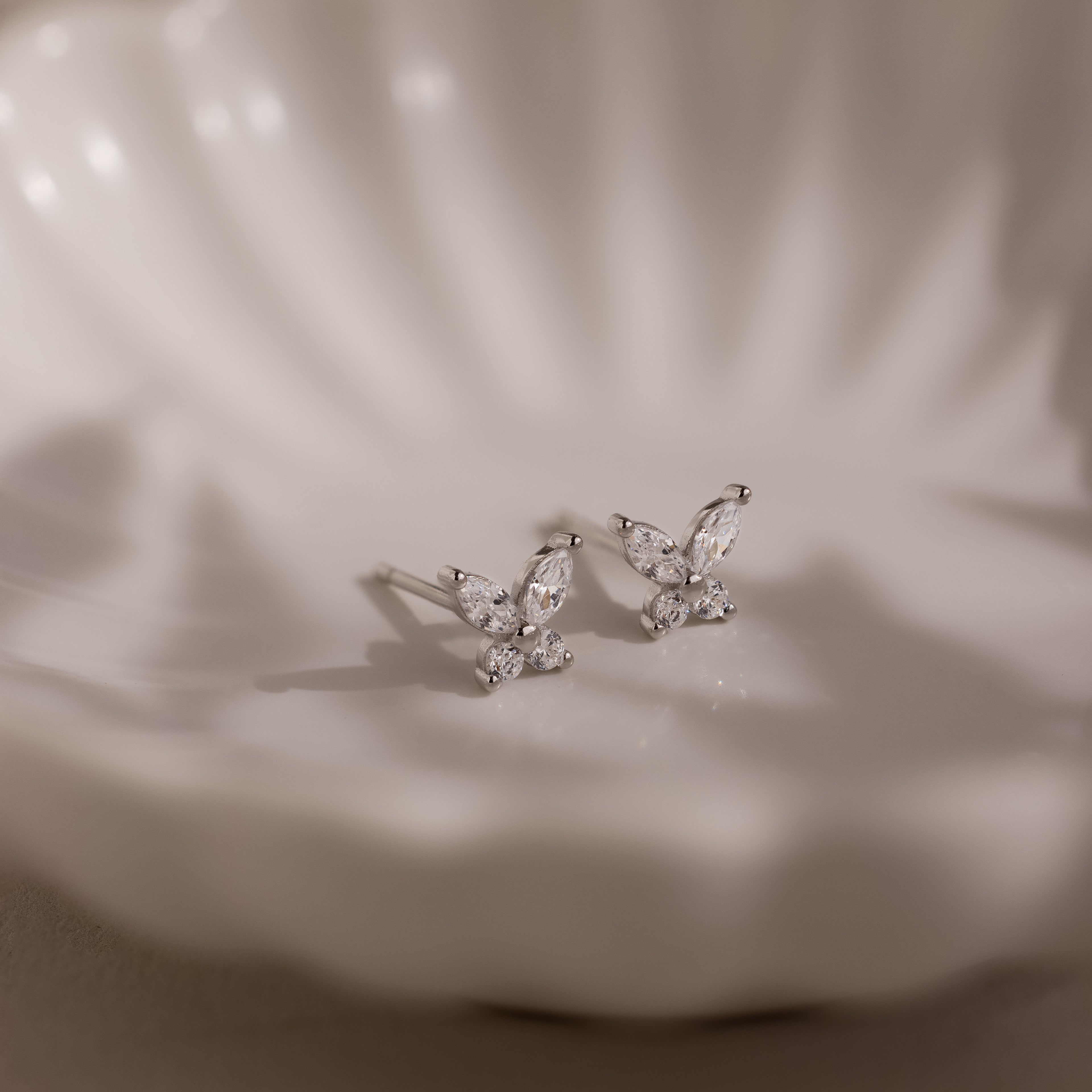 Silver butterfly-shaped earrings on a white jewelry dish