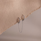 Silver double hoop earrings with chain detail on a textured beige surface