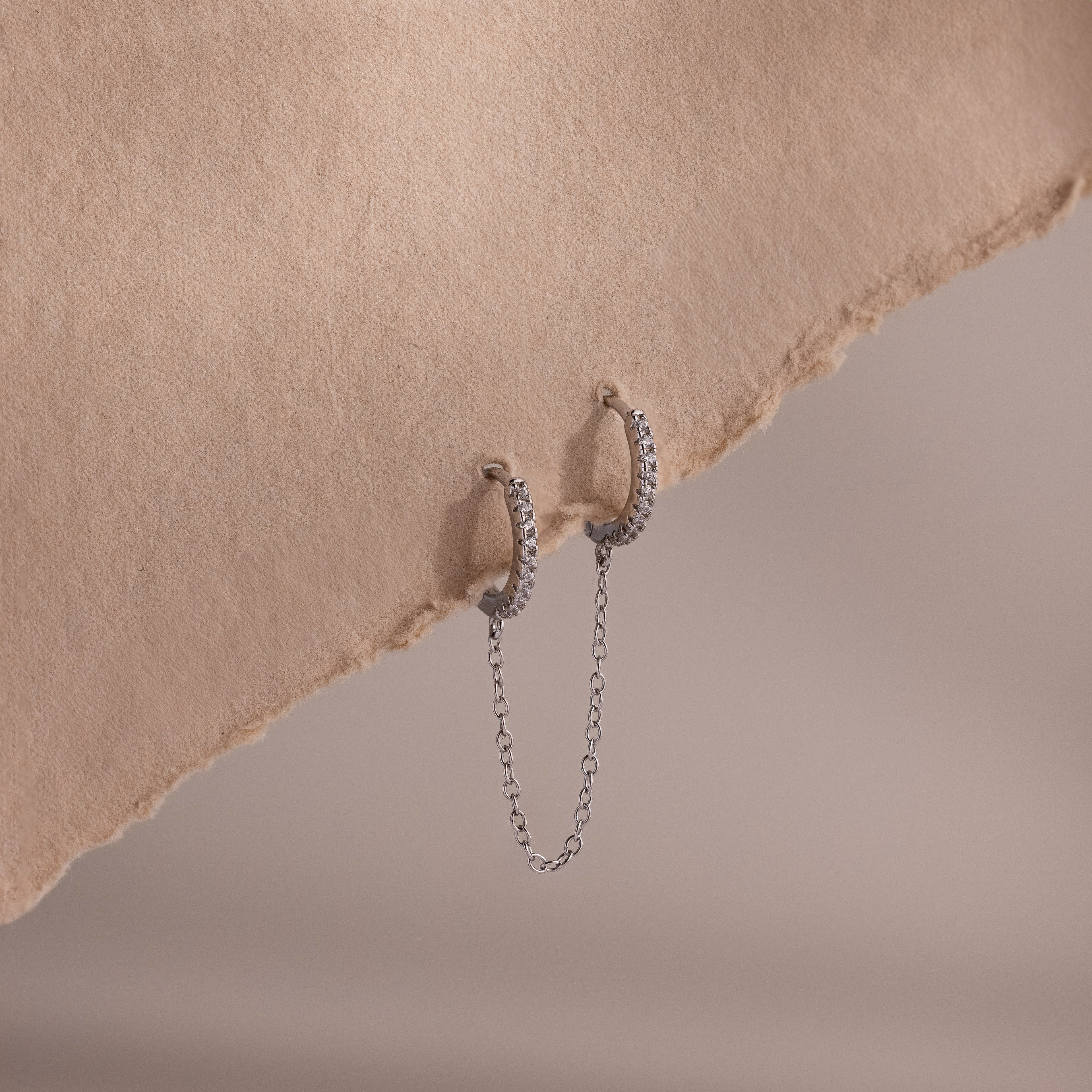 Silver double hoop earrings with chain detail on a textured beige surface
