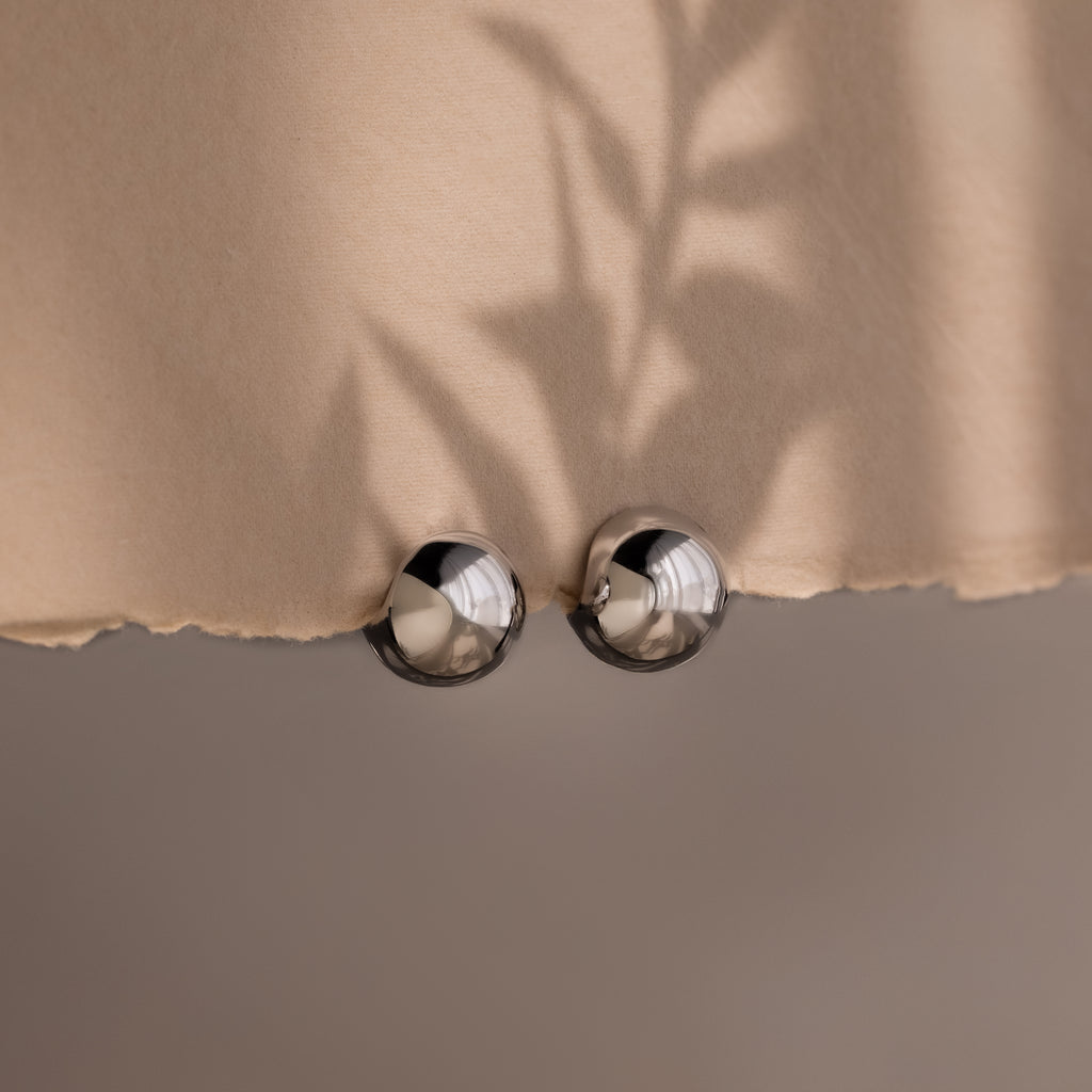Close-up of a beige fabric with metallic spherical hoop earrings on a neutral background