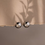 Close-up of a beige fabric with metallic spherical hoop earrings on a neutral background