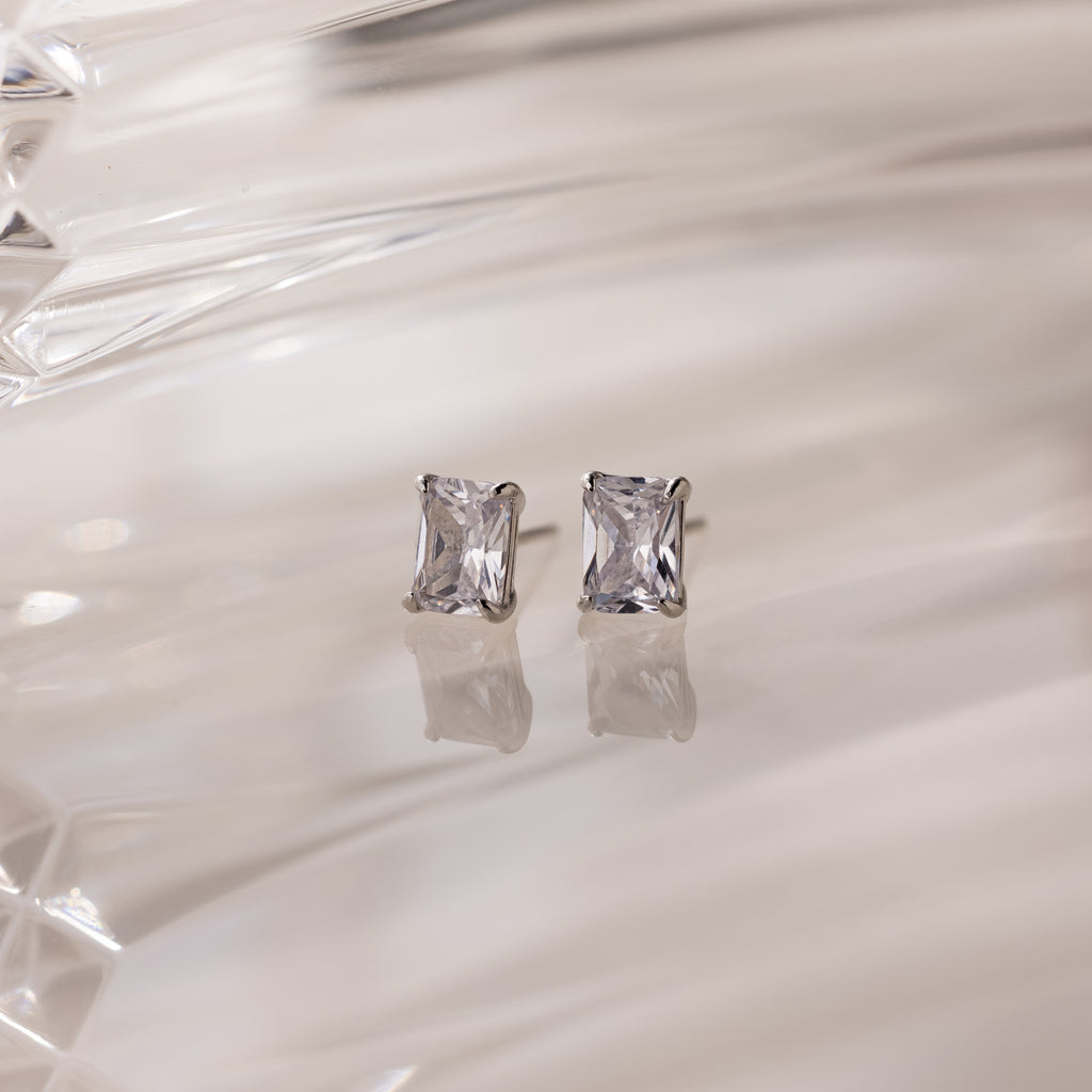 Silver stud earrings with clear rectangular gemstones on a white fabric background