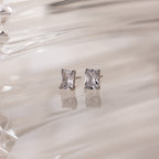 Silver stud earrings with clear rectangular gemstones on a white fabric background