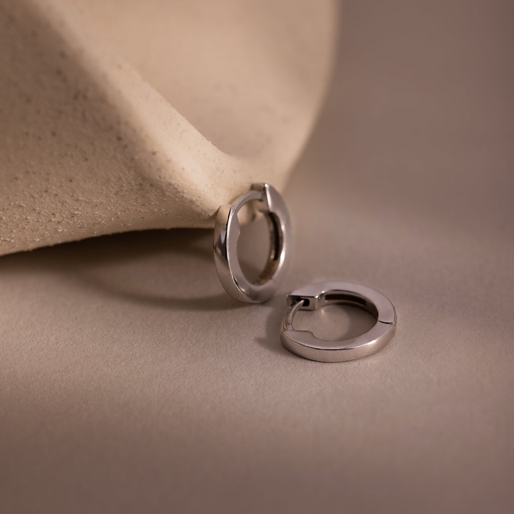 Two silver huggie hoop earrings on a beige fabric background