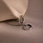 Two silver huggie hoop earrings on a beige fabric background