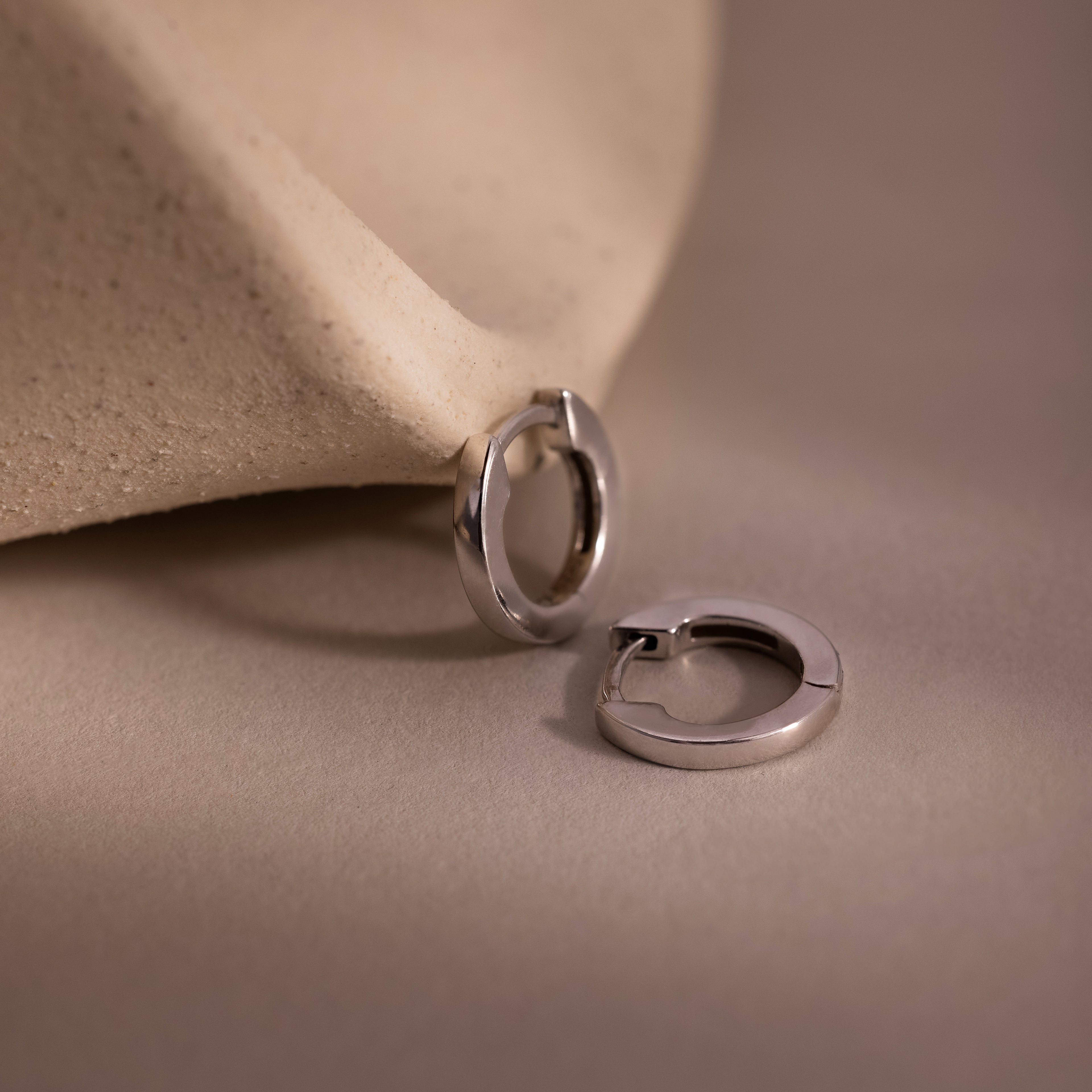 Two silver huggie hoop earrings on a beige fabric background