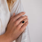 Close-up of a hand wearing the Midnight Hour Onyx Ring with an adjustable band, resting on a white long-sleeve shirt.