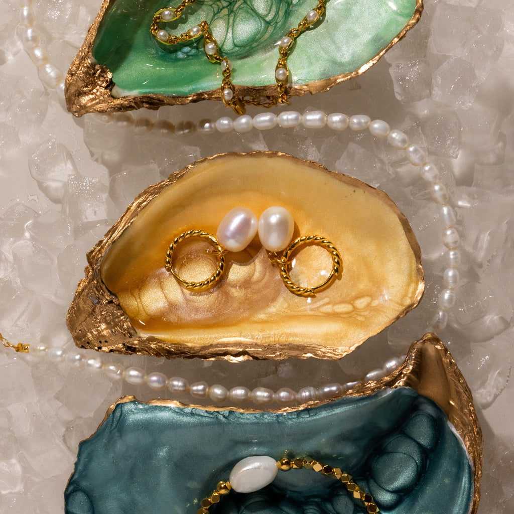 Gold-edged oyster shells display pearl jewelry, rings, and Twisted Pearl Hoops in 18K Gold, surrounded by ice and a pearl necklace.