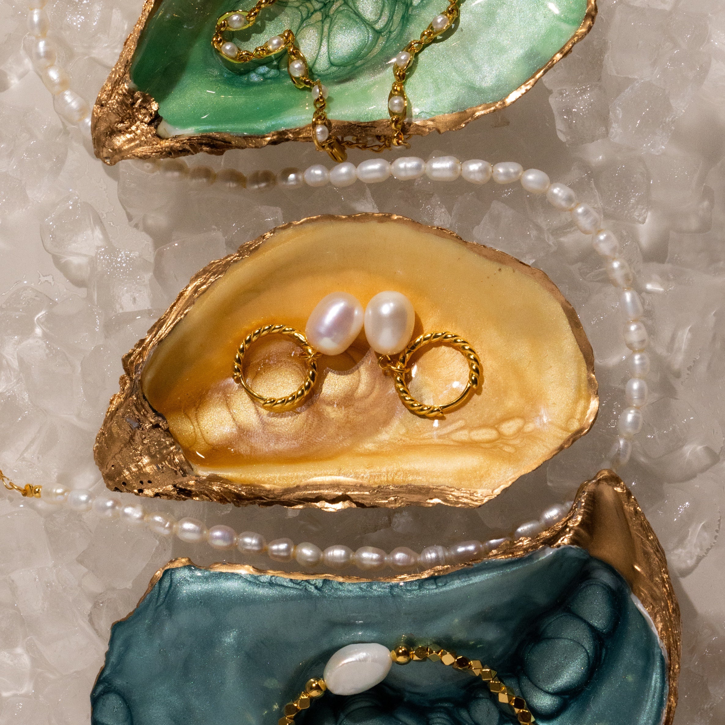 Gold-edged oyster shells display pearl jewelry, rings, and Twisted Pearl Hoops in 18K Gold, surrounded by ice and a pearl necklace.