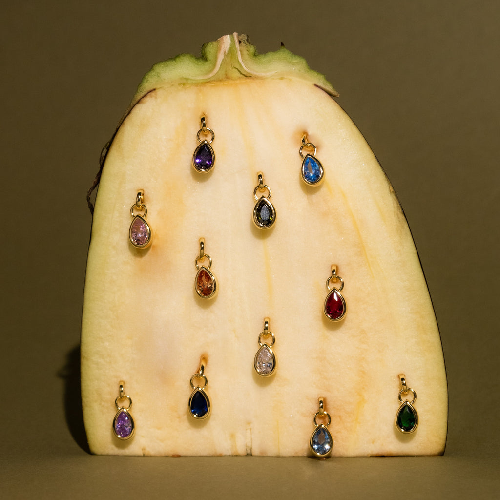 A Teardrop Blue Zircon Charm in a gold bezel setting is displayed on a vertically cut banana against a plain background.