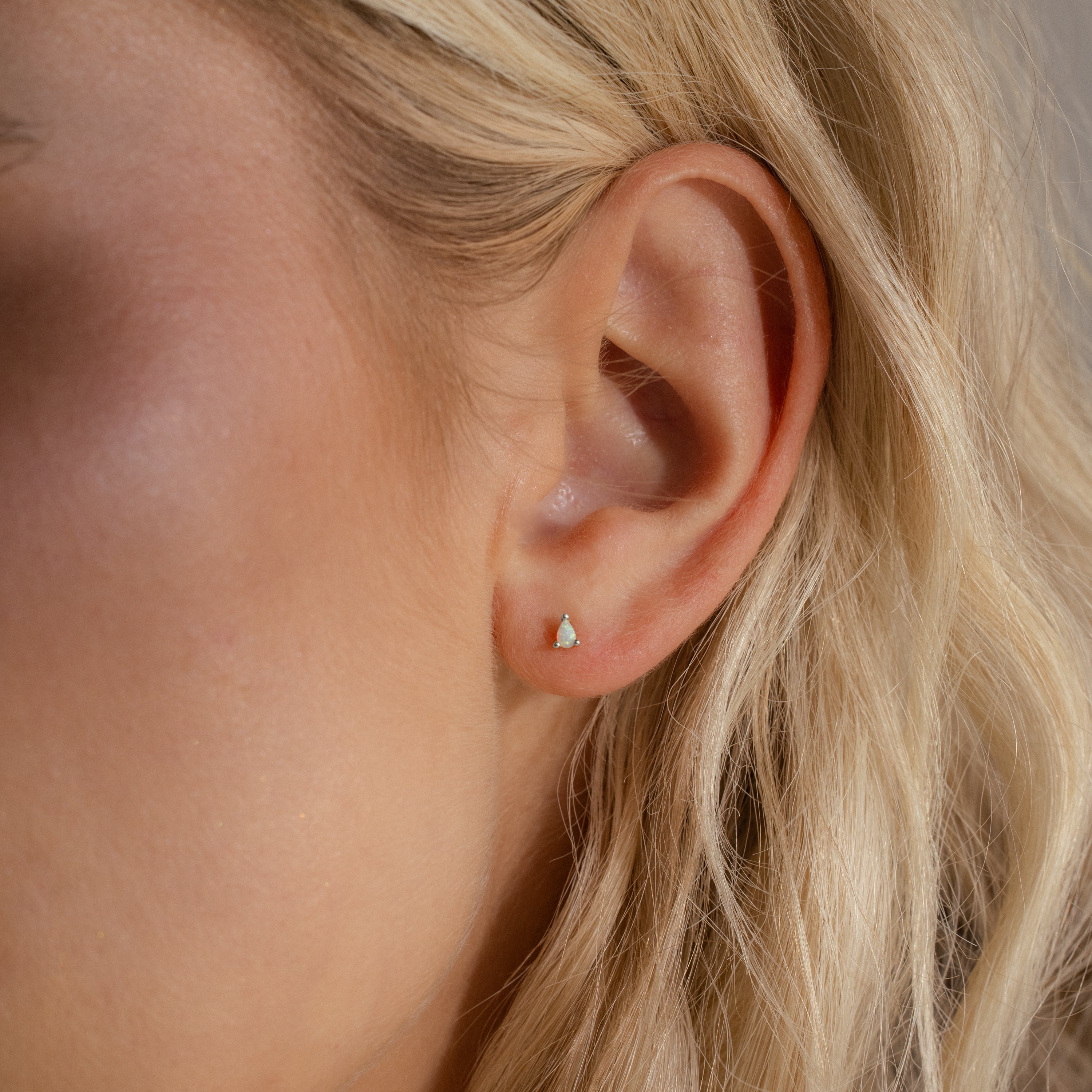 A silver pear opal stud worn on a woman’s earlobe, subtly catching the light for a soft, iridescent glow.