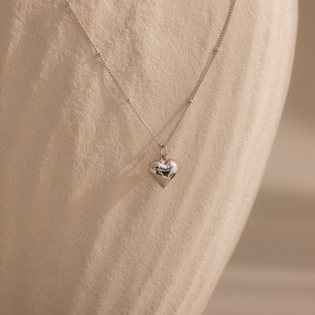 Silver Puff Heart Pendant Necklace displayed against a textured, ivory-toned background.
