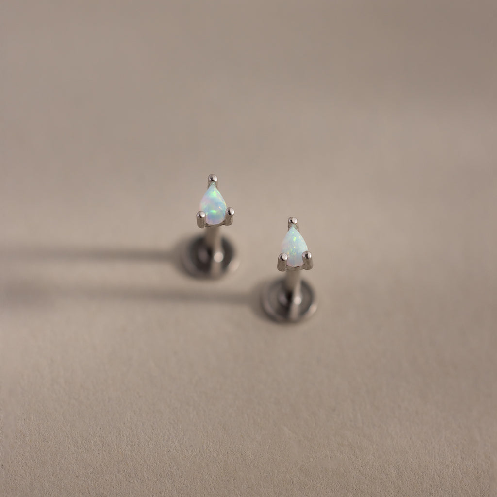 Teardrop opal flatback studs with silver prong settings on a soft beige surface.