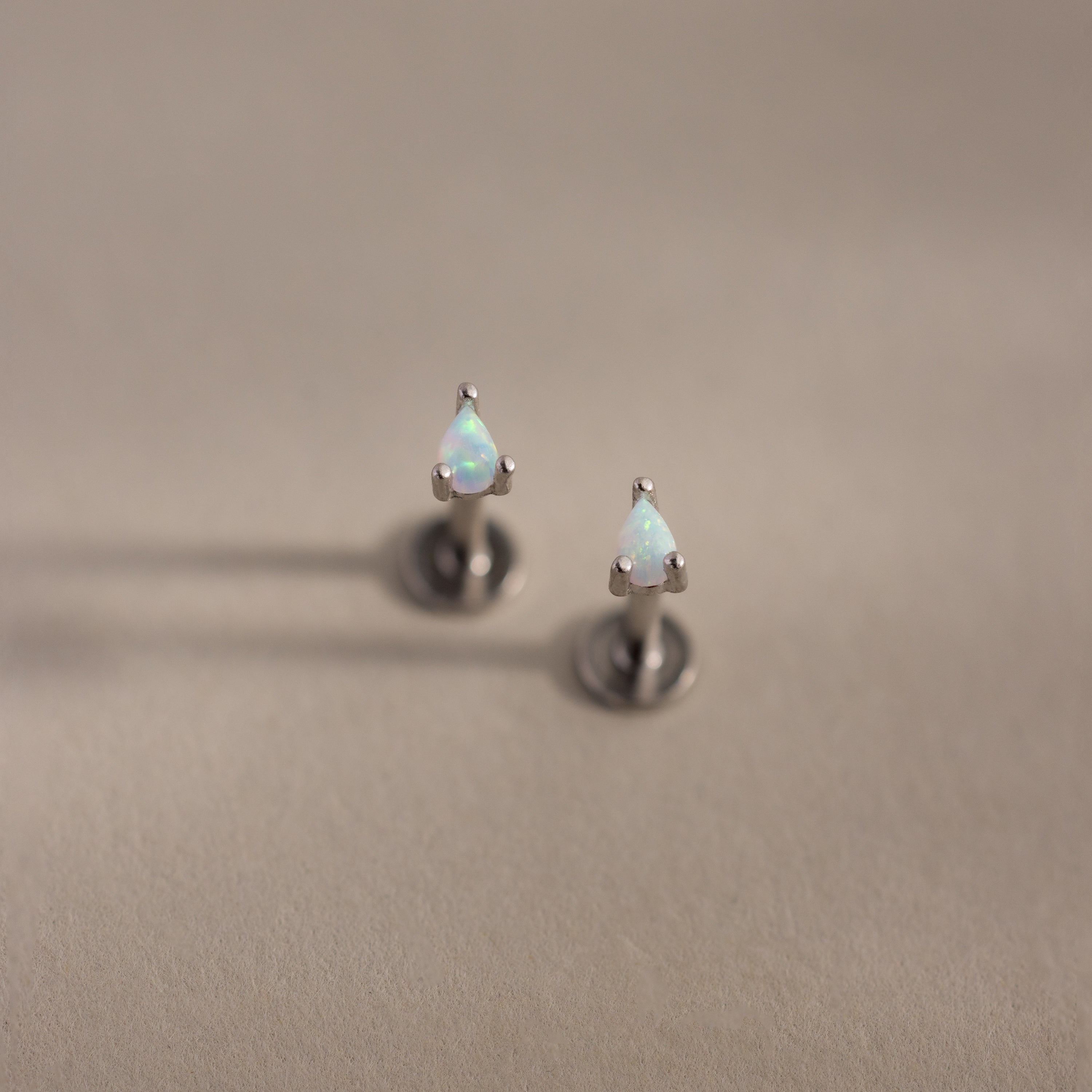 Teardrop opal flatback studs with silver prong settings on a soft beige surface.