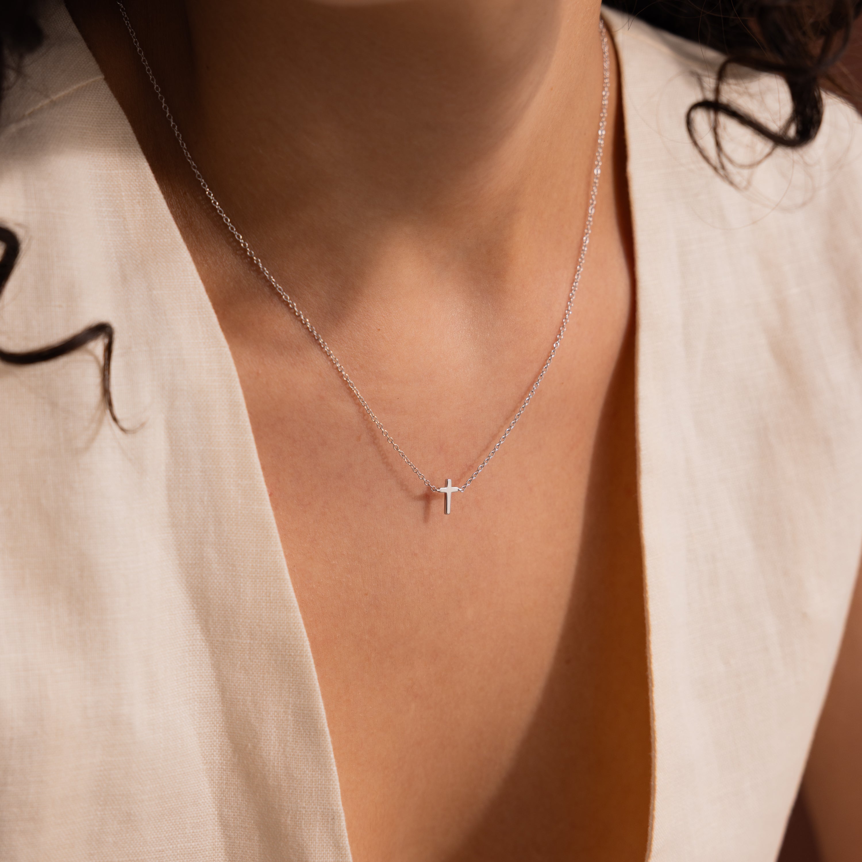 Model wearing a dainty silver cross charm necklace.