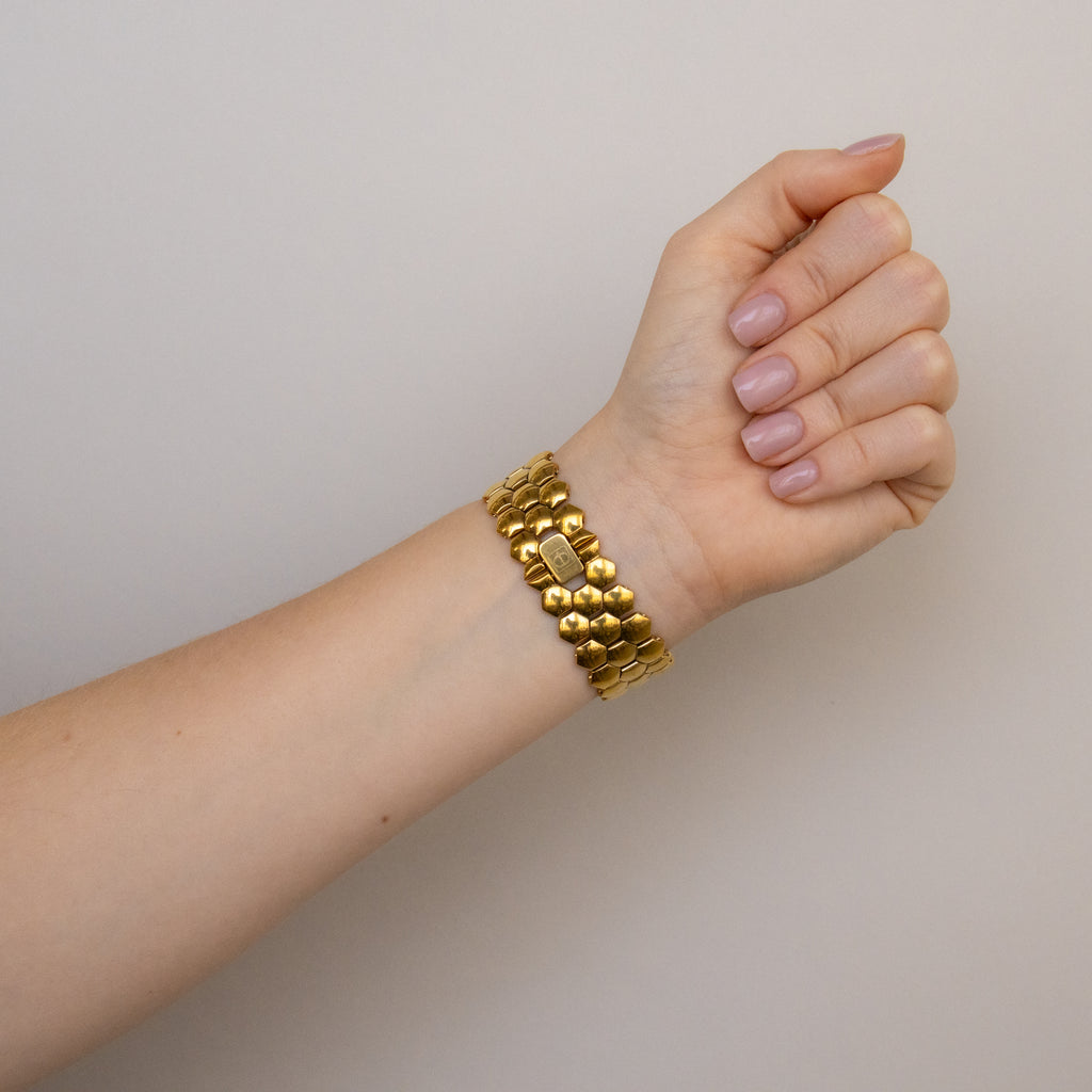 A hand with neatly manicured nails wears a chunky gold bracelet and the Vintage Christian Bernard Honeycomb Gold Watch against a neutral background.