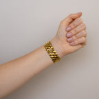 A hand with neatly manicured nails wears a chunky gold bracelet and the Vintage Christian Bernard Honeycomb Gold Watch against a neutral background.