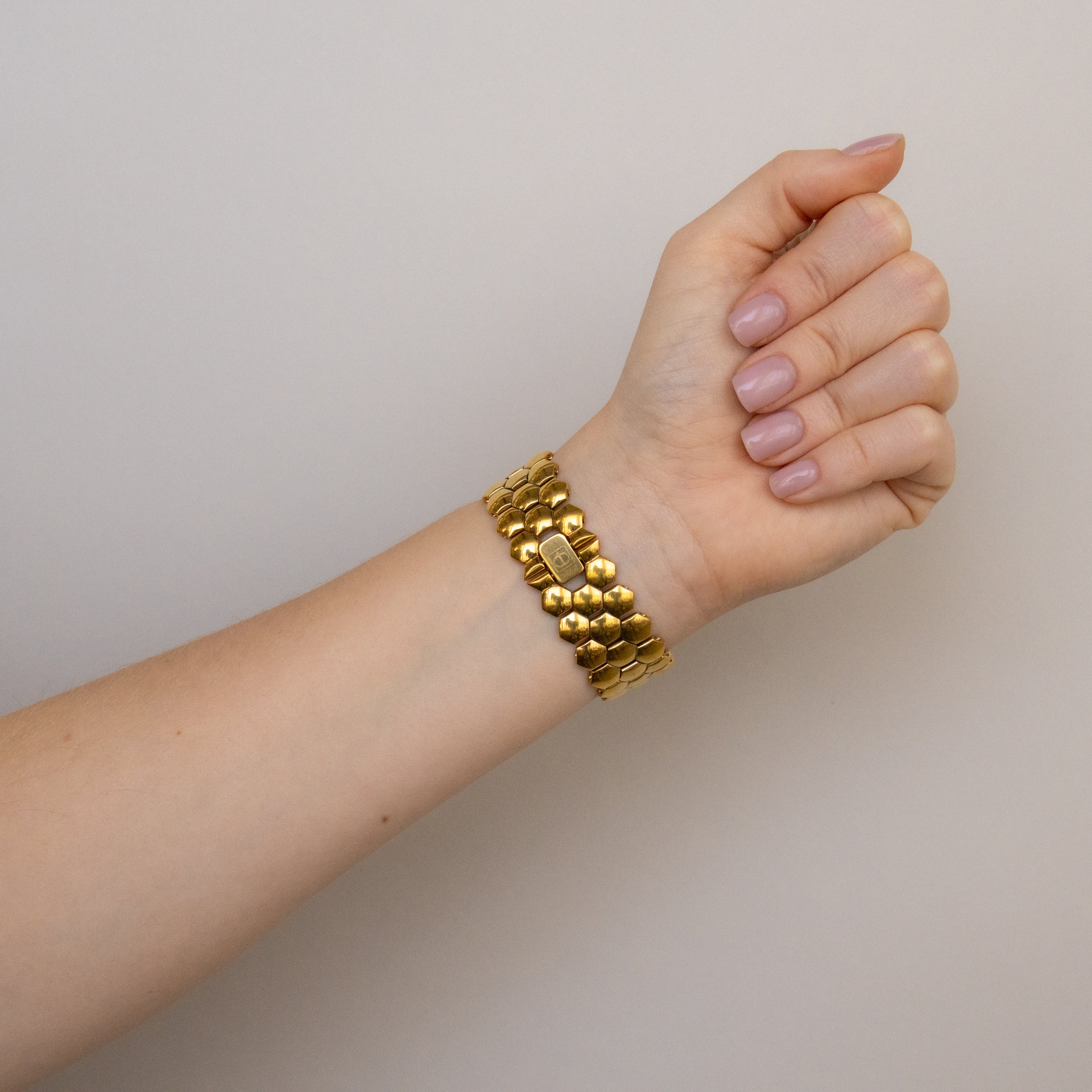 A hand with neatly manicured nails wears a chunky gold bracelet and the Vintage Christian Bernard Honeycomb Gold Watch against a neutral background.