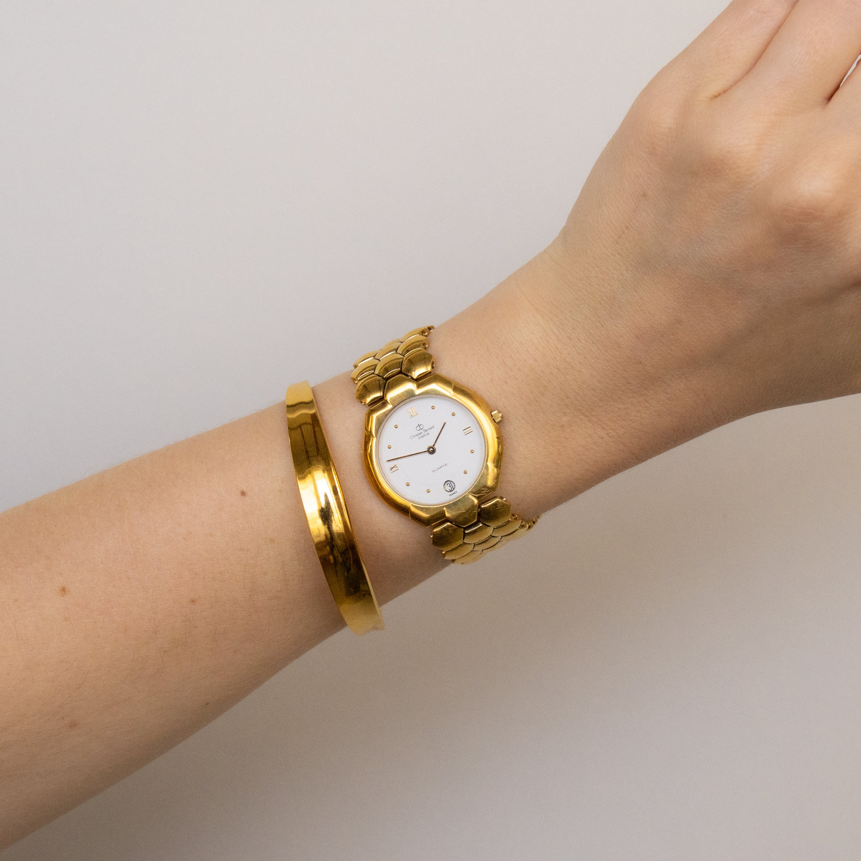 A Vintage Christian Bernard Honeycomb Gold Watch paired with a gold bracelet is worn on a wrist, shown against a plain light background.