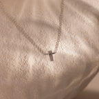 Dainty silver cross charm necklace displayed against a neutral stone surface.
