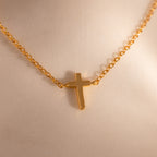 Close-up of a dainty gold cross charm necklace against a neutral surface.