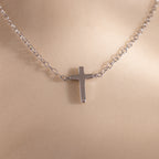Close-up of a dainty silver cross charm necklace displayed against a neutral surface.