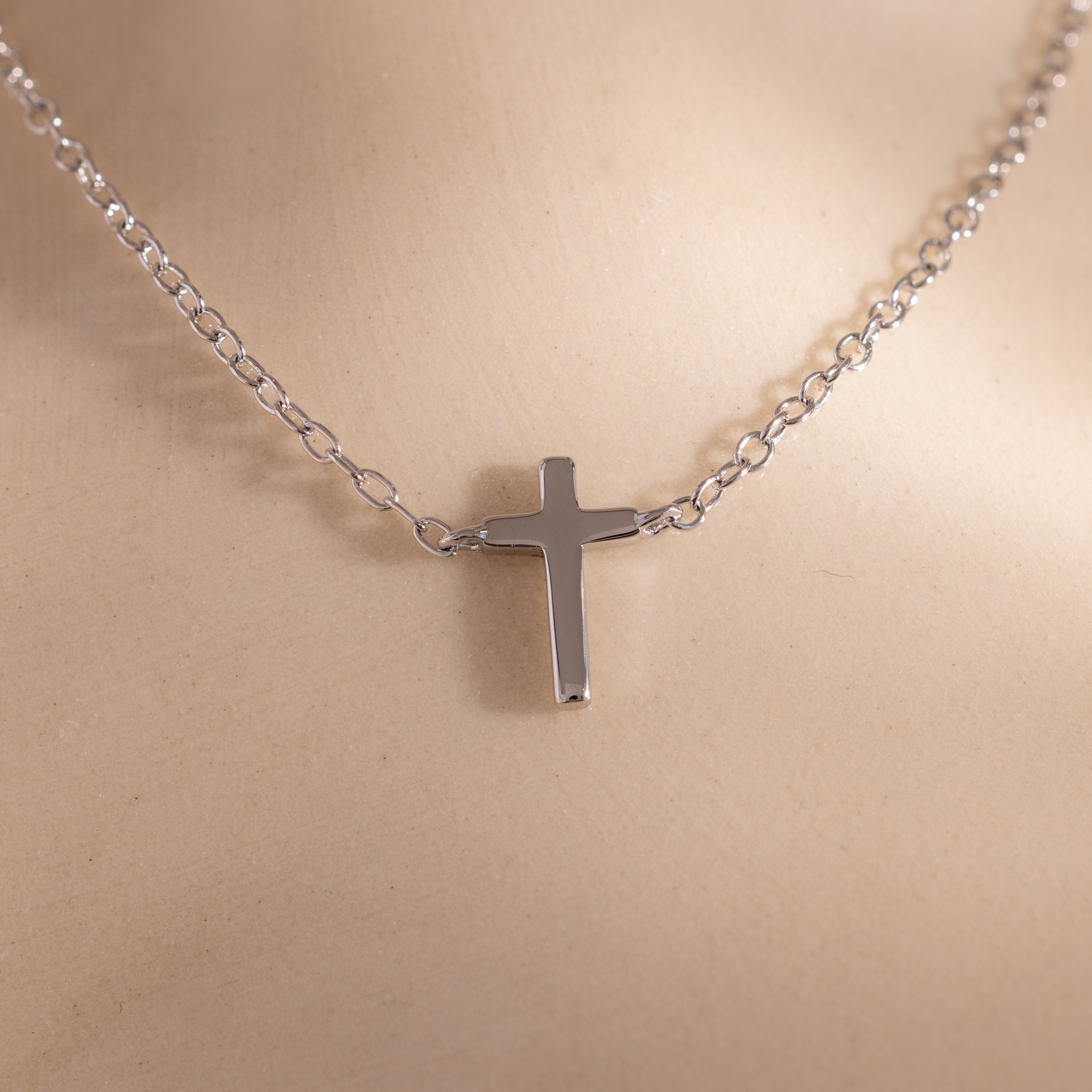 Close-up of a dainty silver cross charm necklace displayed against a neutral surface.