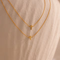 Two dainty gold cross charm necklaces in 16 and 18 inches, displayed against a neutral stone surface.