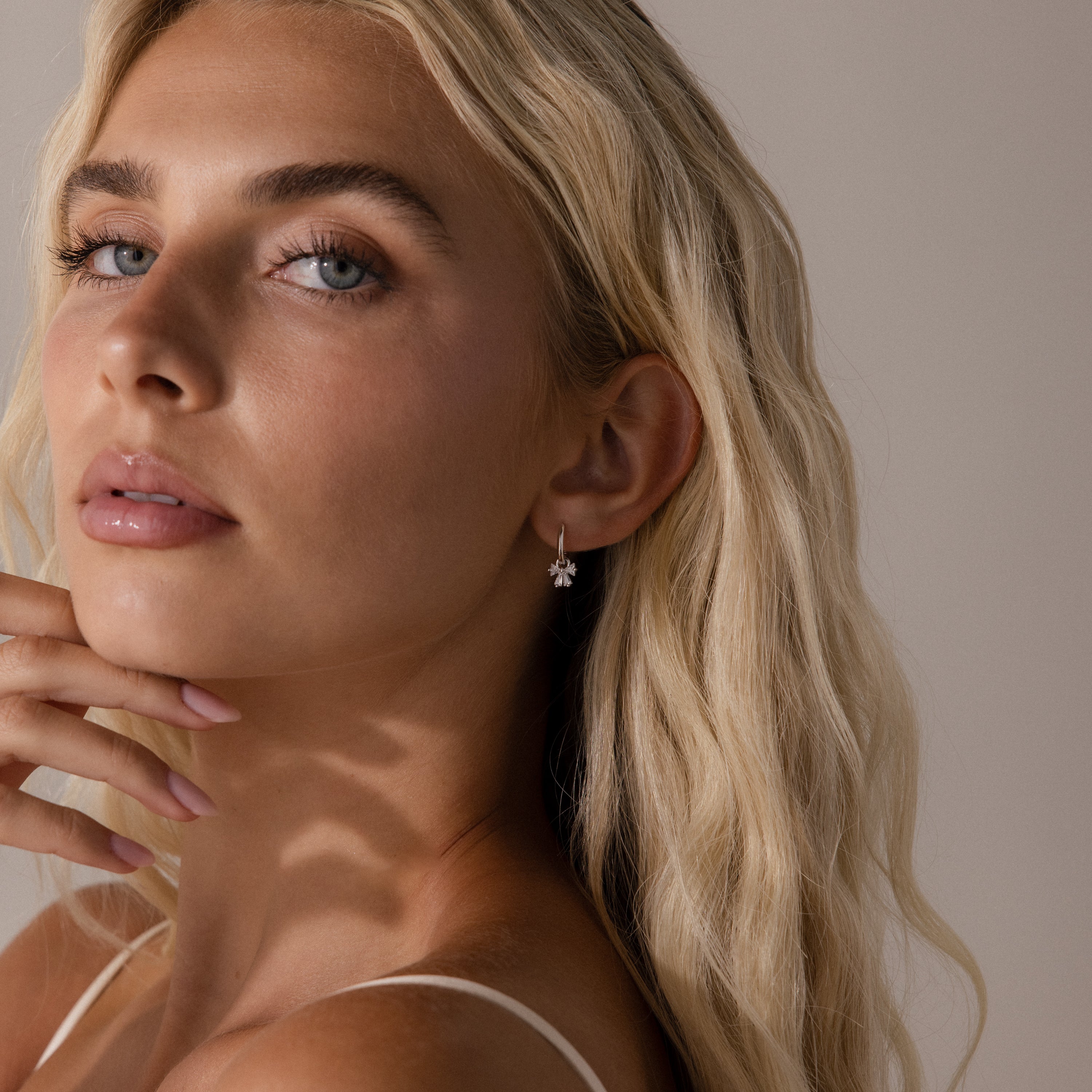 Close-up of silver hoop earrings with crystal-studded bow charms, displayed on a neutral background.